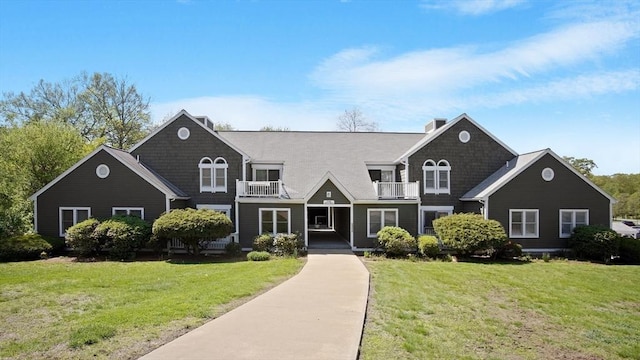 view of front facade with a balcony, a front yard, and a chimney