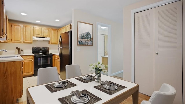 kitchen featuring black appliances, under cabinet range hood, a sink, light countertops, and light brown cabinets
