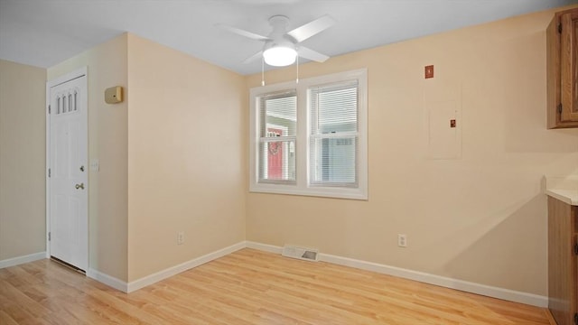 empty room featuring ceiling fan, light wood finished floors, baseboards, and electric panel