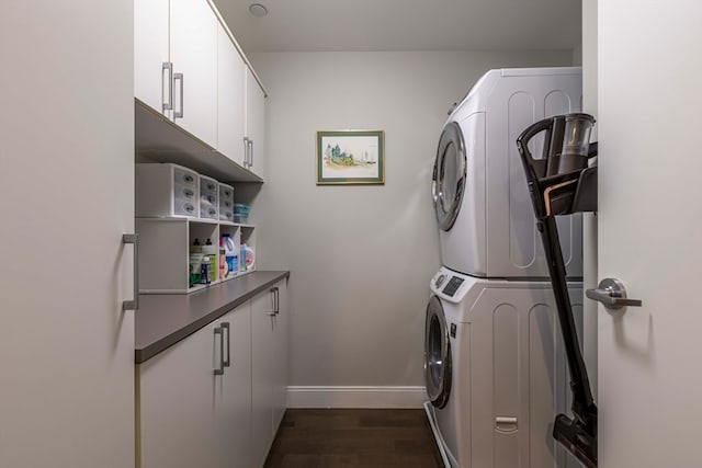 clothes washing area featuring stacked washing maching and dryer, dark hardwood / wood-style flooring, and cabinets