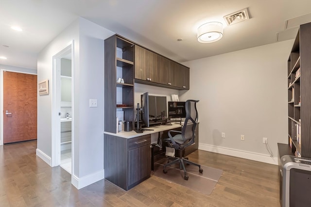 home office with dark wood-type flooring and built in desk