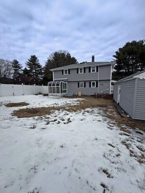 snow covered house with a sunroom and fence