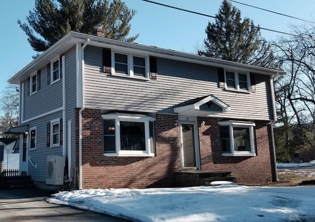 colonial-style house featuring ac unit, a chimney, and brick siding