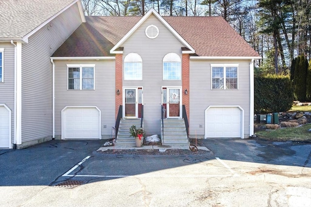 raised ranch with driveway, roof with shingles, an attached garage, and entry steps