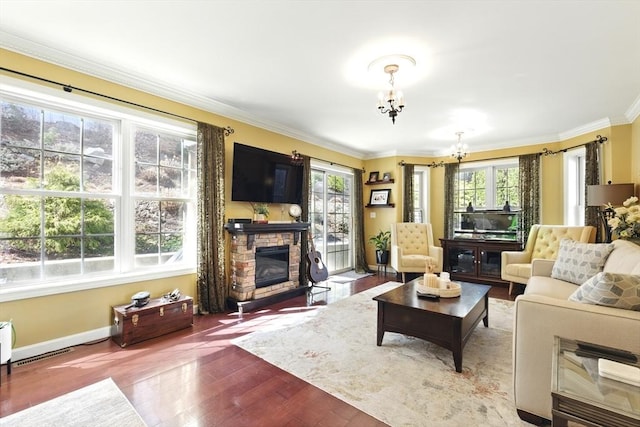 living area with wood finished floors, a stone fireplace, crown molding, baseboards, and a chandelier