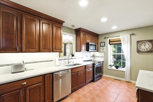 kitchen featuring light tile patterned flooring, a sink, decorative backsplash, hanging light fixtures, and appliances with stainless steel finishes