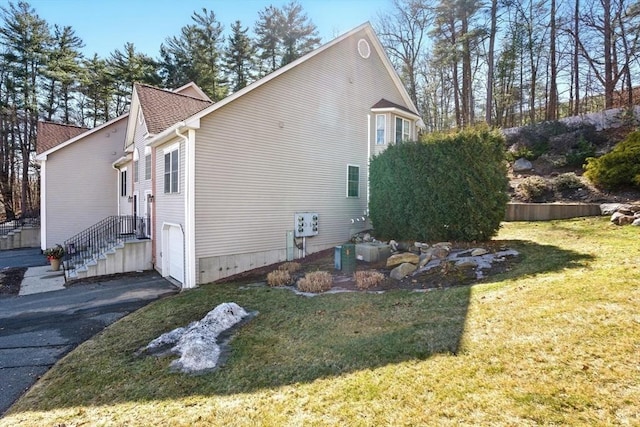 view of home's exterior featuring aphalt driveway, a yard, a garage, and roof with shingles