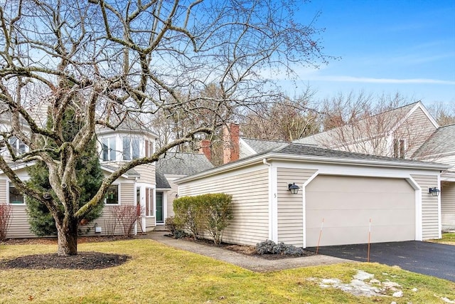 view of side of home with roof with shingles, a chimney, a yard, a garage, and driveway