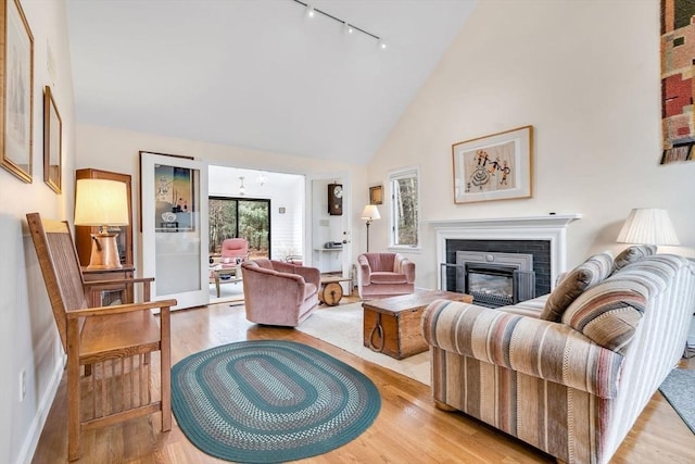 living area featuring a glass covered fireplace, high vaulted ceiling, light wood-style flooring, and track lighting