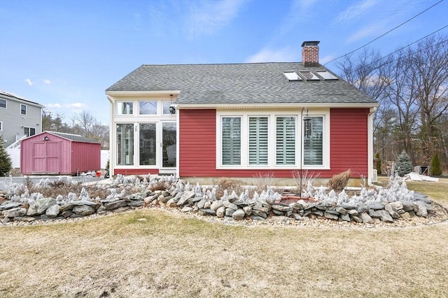 back of house featuring a shingled roof, a chimney, a storage shed, a yard, and an outbuilding