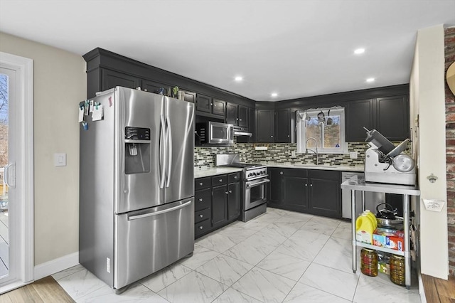 kitchen featuring light countertops, appliances with stainless steel finishes, dark cabinetry, marble finish floor, and a sink