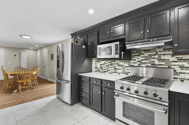 kitchen with under cabinet range hood, marble finish floor, appliances with stainless steel finishes, and dark cabinetry