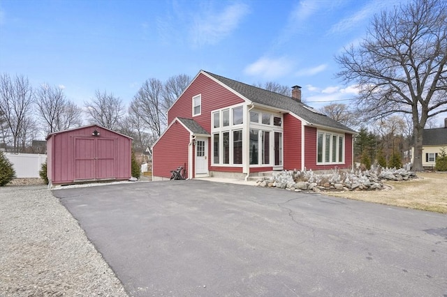 exterior space featuring an outbuilding, fence, a shed, a shingled roof, and a chimney