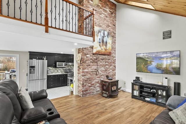 living room with light wood-style floors, a towering ceiling, and a wood stove