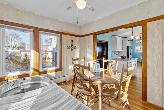 dining space with a baseboard radiator, ceiling fan with notable chandelier, and light hardwood / wood-style floors