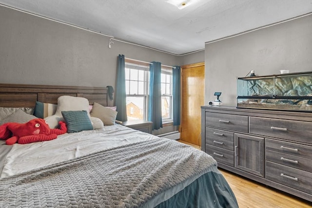 bedroom with a baseboard heating unit and light wood-type flooring