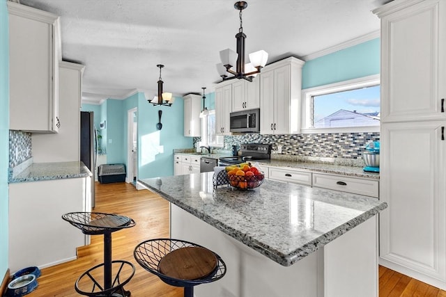 kitchen featuring white cabinetry, hanging light fixtures, appliances with stainless steel finishes, a kitchen island, and light stone countertops