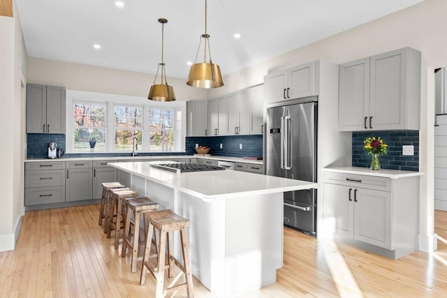 kitchen featuring tasteful backsplash, gray cabinetry, a kitchen island, and appliances with stainless steel finishes