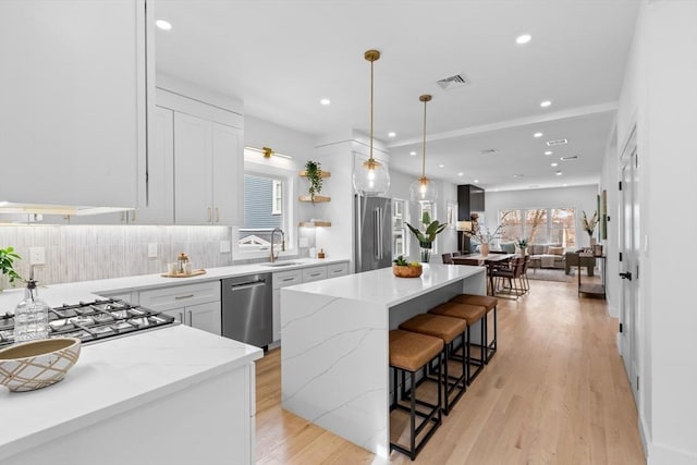 kitchen featuring a kitchen island, appliances with stainless steel finishes, pendant lighting, sink, and white cabinets