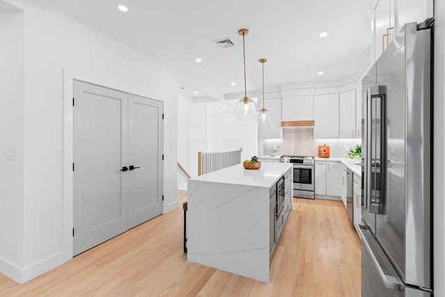 kitchen with a kitchen island, pendant lighting, white cabinets, stainless steel appliances, and light stone countertops