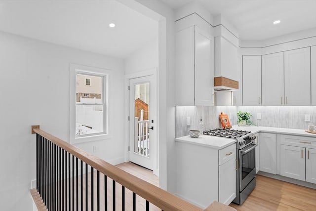 kitchen with white cabinetry, gas range, light wood-type flooring, and decorative backsplash