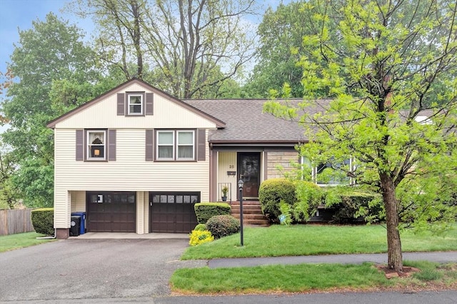 split level home featuring a garage, asphalt driveway, and roof with shingles