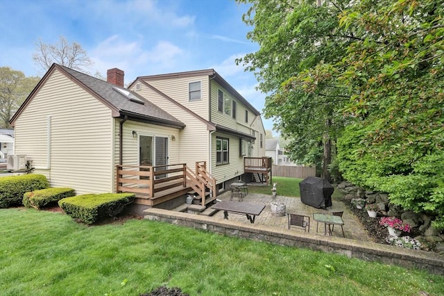 rear view of property with a chimney, a wooden deck, a patio area, a lawn, and roof with shingles