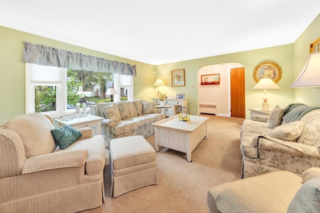 living room featuring radiator heating unit, light carpet, and arched walkways
