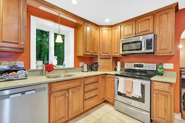 kitchen featuring appliances with stainless steel finishes, a sink, light tile patterned floors, decorative light fixtures, and brown cabinets