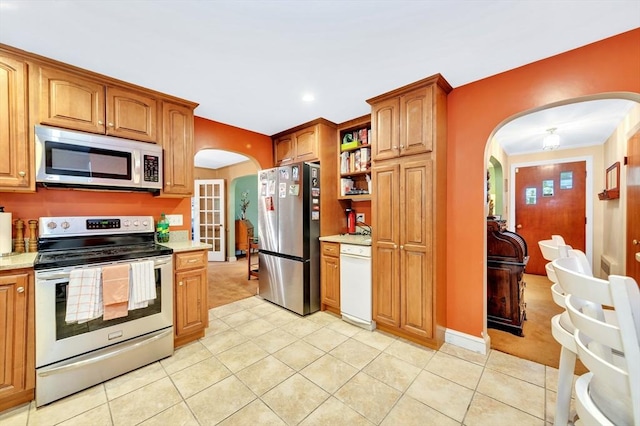 kitchen featuring stainless steel appliances, arched walkways, light carpet, light tile patterned floors, and recessed lighting
