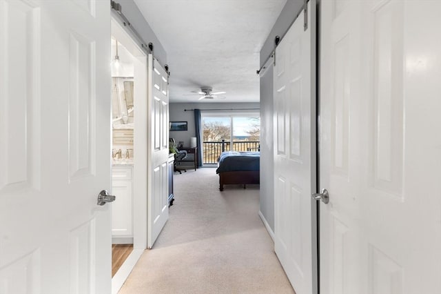 hallway featuring light colored carpet and a barn door