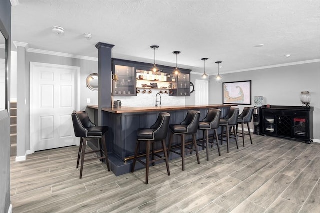 bar with wood counters, decorative light fixtures, sink, decorative backsplash, and crown molding