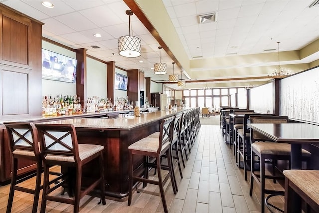 bar with a drop ceiling, hanging light fixtures, and light stone countertops