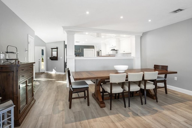 dining space with vaulted ceiling, light hardwood / wood-style floors, and ornate columns