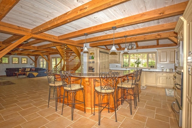 kitchen with light stone counters, hanging light fixtures, beam ceiling, cream cabinetry, and a kitchen breakfast bar