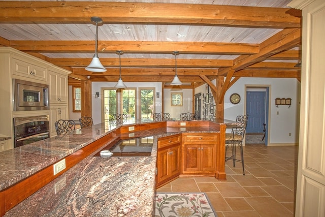 kitchen featuring hanging light fixtures, beam ceiling, appliances with stainless steel finishes, a breakfast bar, and dark stone counters