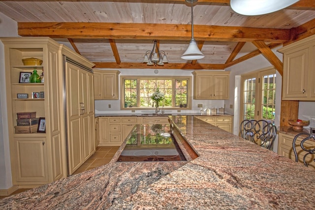 kitchen featuring dark stone countertops, vaulted ceiling with beams, cream cabinetry, and a wealth of natural light