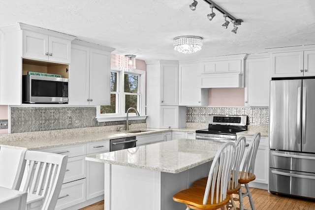 kitchen with sink, white cabinets, a center island, light stone counters, and stainless steel appliances