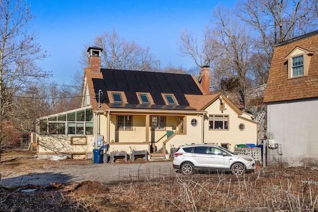 view of front facade with a sunroom, roof mounted solar panels, and a chimney