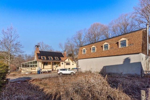 rear view of property with a shingled roof, a sunroom, and a chimney