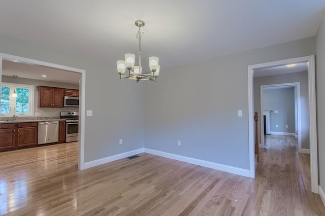 unfurnished dining area featuring a notable chandelier, visible vents, light wood-style floors, a sink, and baseboards