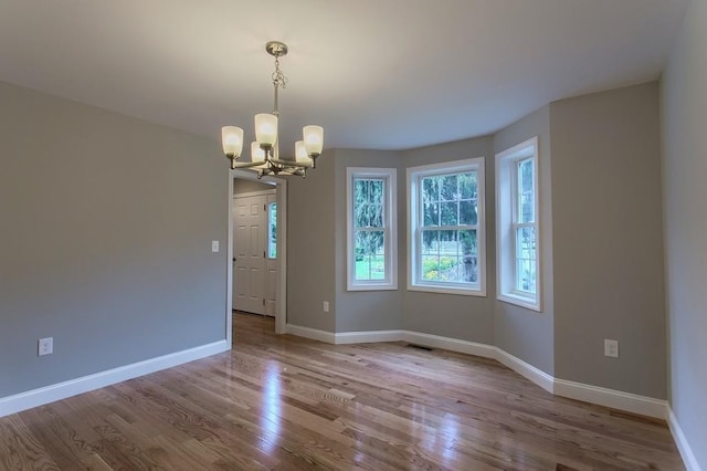 unfurnished room with an inviting chandelier, visible vents, baseboards, and wood finished floors