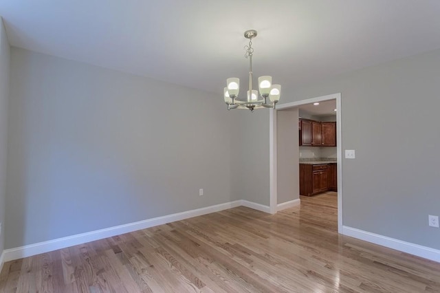 unfurnished dining area with a chandelier, light wood-type flooring, and baseboards