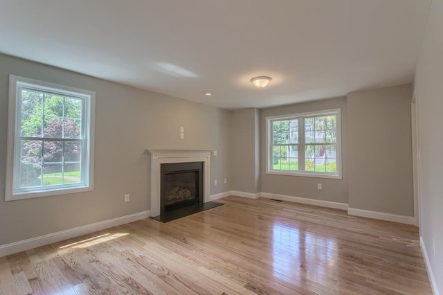 unfurnished living room featuring plenty of natural light, baseboards, wood finished floors, and a fireplace with flush hearth