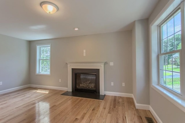 unfurnished living room featuring a fireplace with flush hearth, visible vents, plenty of natural light, and wood finished floors