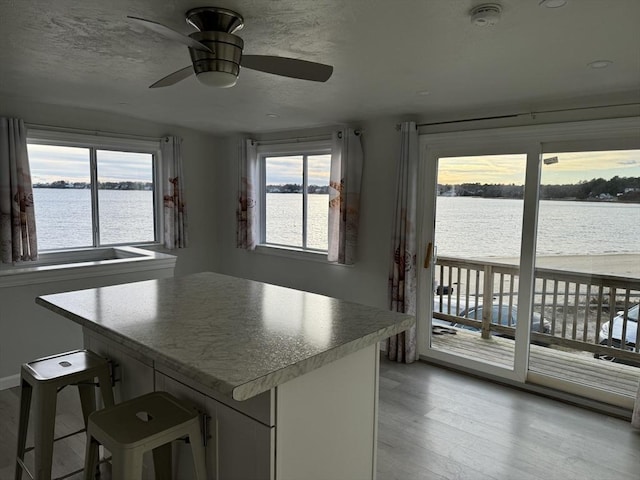 kitchen with ceiling fan, a kitchen island, a breakfast bar, a water view, and light wood-type flooring