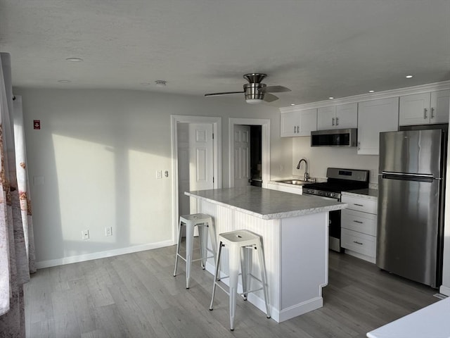 kitchen with a breakfast bar, stainless steel appliances, sink, a center island, and white cabinetry