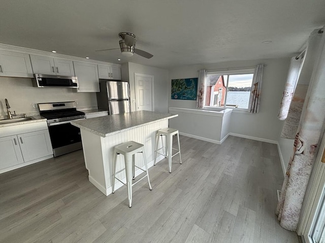 kitchen with white cabinets, ceiling fan, a kitchen island, a kitchen bar, and stainless steel appliances