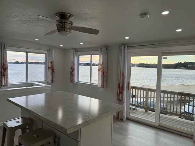 kitchen featuring a kitchen breakfast bar, a water view, light hardwood / wood-style flooring, ceiling fan, and a kitchen island