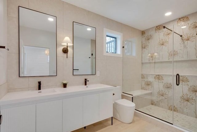 bathroom featuring toilet, wood finished floors, tile walls, a shower stall, and double vanity